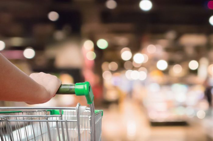 woman hand hold supermarket shopping cart with Abstract grocery store shelves blurred defocused background with bokeh light