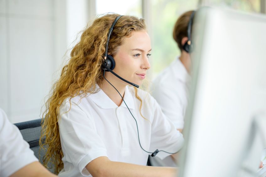 An individual wearing a headset and sitting in front of a computer monitor in an office setting