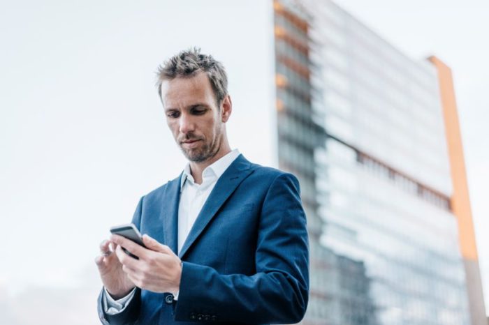 man checking phone in front of building