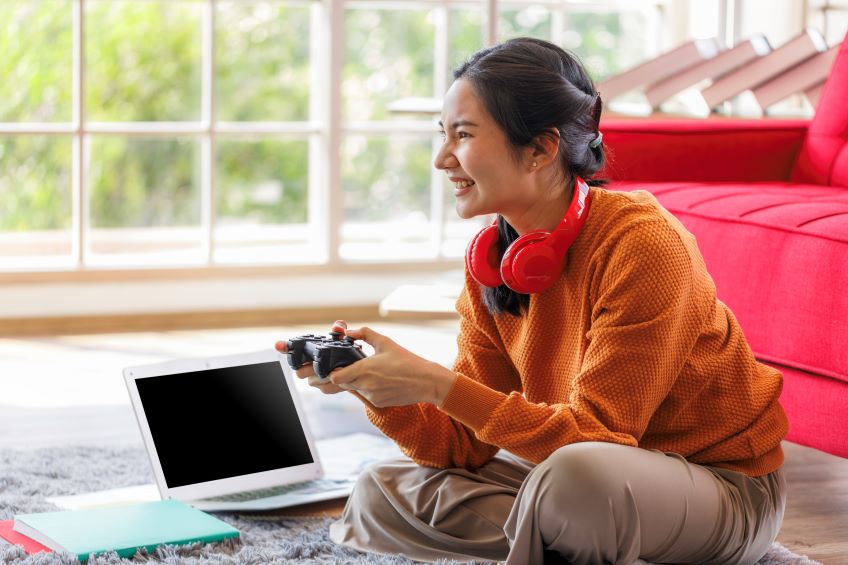woman sits on the floor with a game controller in hand smiling at the screen