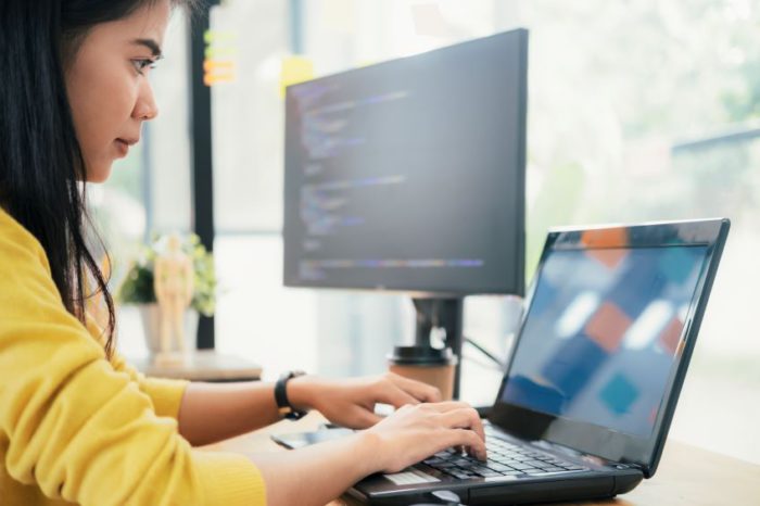 Image of woman working on a laptop with code on a second screen.