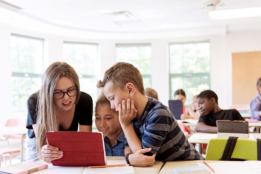 Three students in a classroom looking at a tablet together