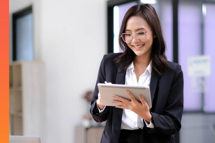 Businessperson standing in an office smiling at a smart tablet.