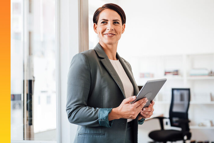 Woman standing in office holding computer tablet looking happy with what she just viewed.