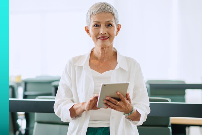 HERO IMAGE ALT TEXT (to be provided before build) Woman stands in an office building and holds a tablet