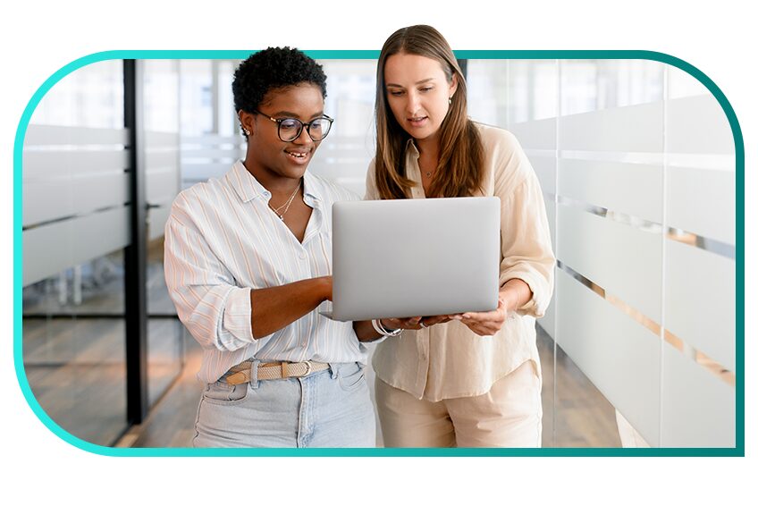 Two people in business attire collaborate on a laptop in an office setting