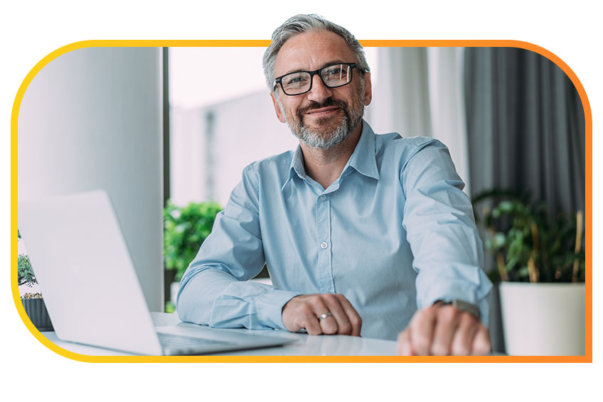 Person in business casual attire smiling and sitting at a desk with a laptop.